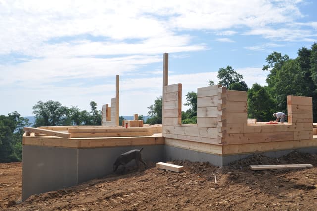 The first courses of log wall stacked two and three high on the deck, square-cut timbers