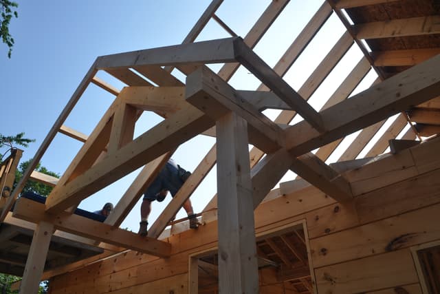 Heavy timber trusses and rafters against a blue sky, seen from below through the open roof