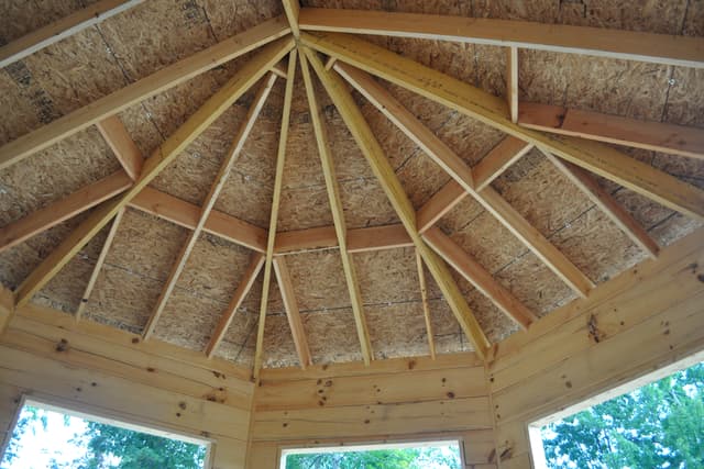 Inside an octagon roof, twelve rafters converging on a central hub, sheathed in board