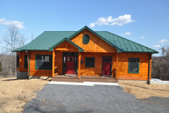 The front elevation of the finished log home in early spring, green metal roof and stained log walls
