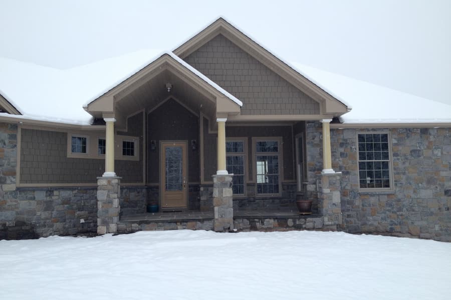 The entry porch straight on in deep snow, both columns and the paneled door centered under the gable