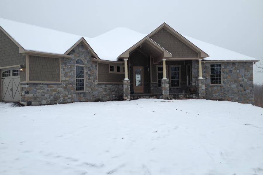 The finished house across snow, entry gable centered between the garage wing and the stone end