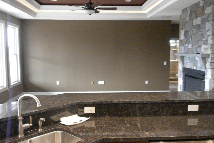 The kitchen counter run and sink, tray ceiling with a fan above and the stone chimney visible past the corner
