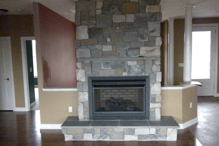A stone fireplace with a raised hearth built out into the room, red and tan walls either side and a glazed door beyond