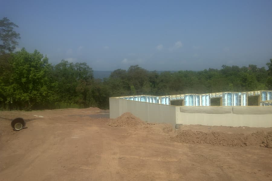 The finished foundation from the far end, earth banked against the near wall, treeline and haze behind