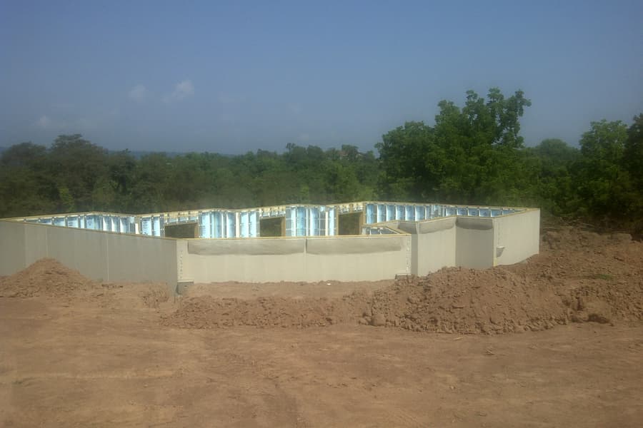 Foundation walls standing on the pad, precast panels with insulation showing between the ribs, the footprint stepping around its corners