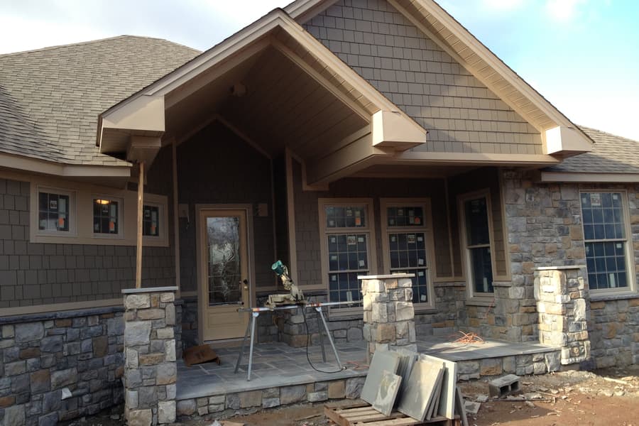 The entry front with its gable and columns, stonework going up and flagstone stacked ready on the ground