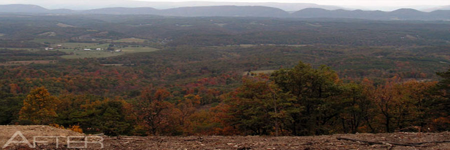 Open cleared ground looking out over a wide valley, wooded ridges running back to the horizon