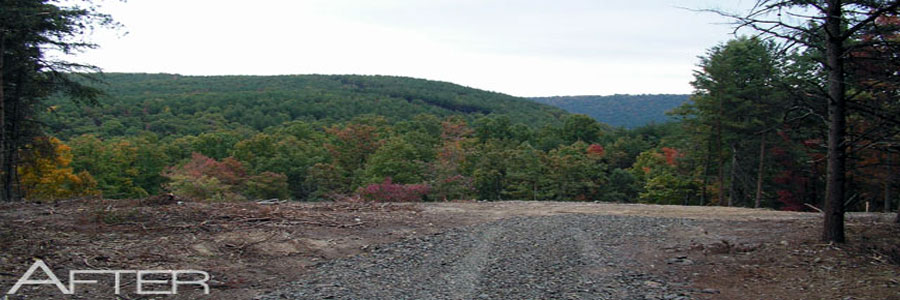 A cleared and graded building pad with fresh gravel, a wooded mountain rising beyond it